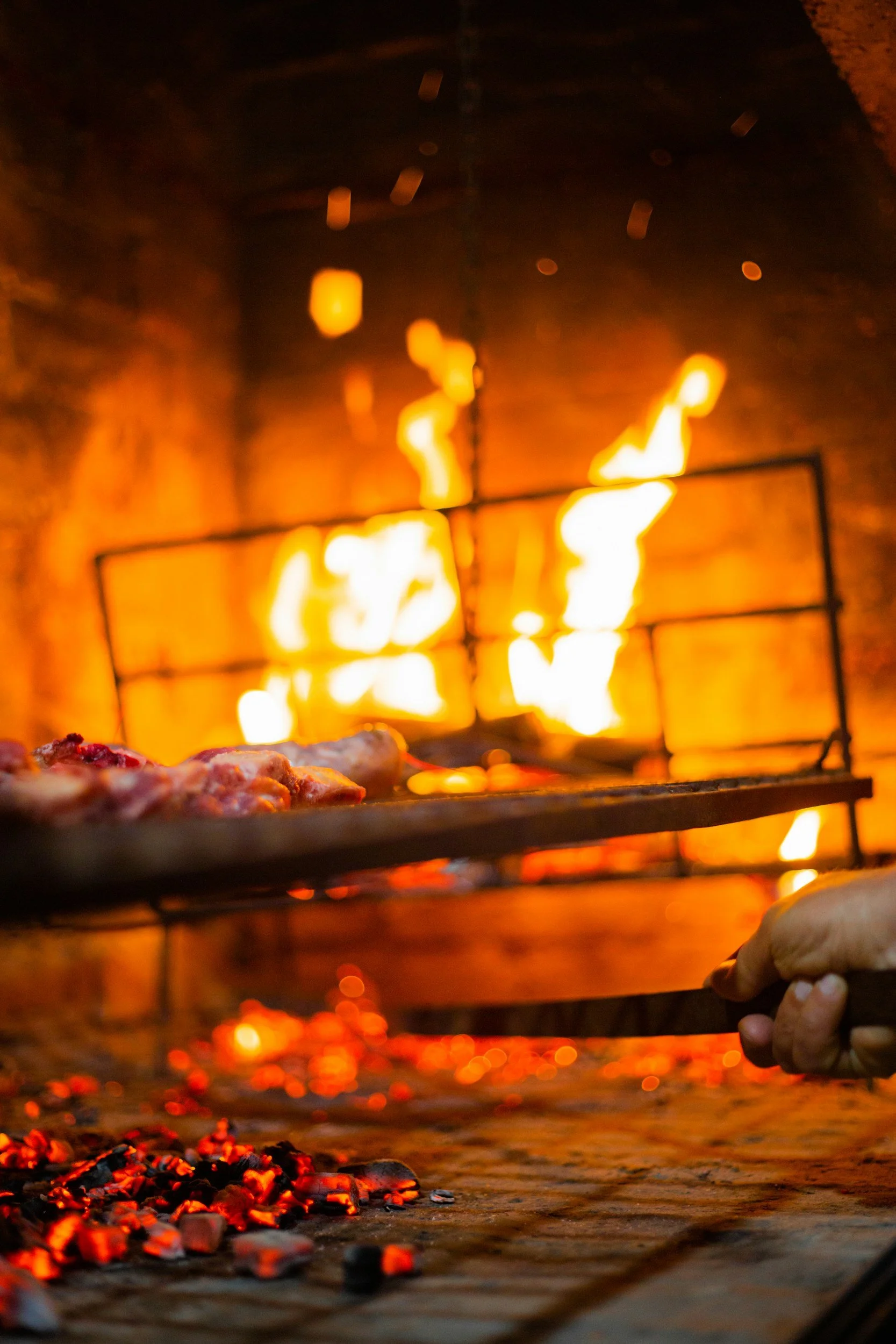 Una pizza cocinándose en el horno de barro, con las llamas y las brasas en primer plano.
